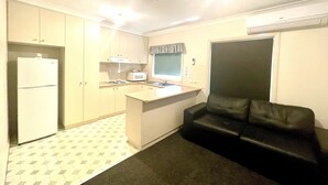 A compact kitchen with a refrigerator, microwave, and stove. There is a black leather couch and a window with a curtain.
