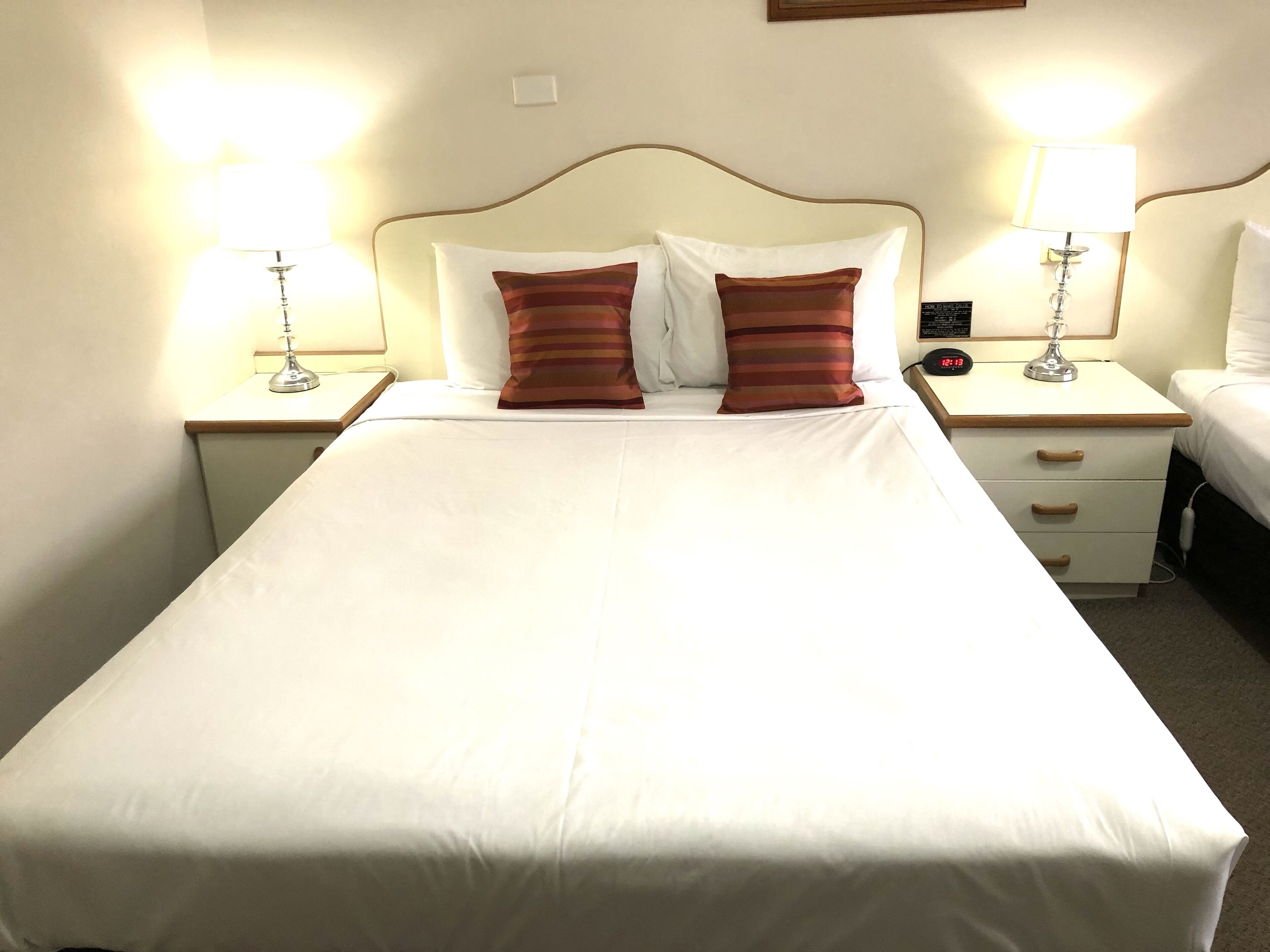 A hotel room with a large bed, two bedside tables, two lamps, and a nightstand with a clock.