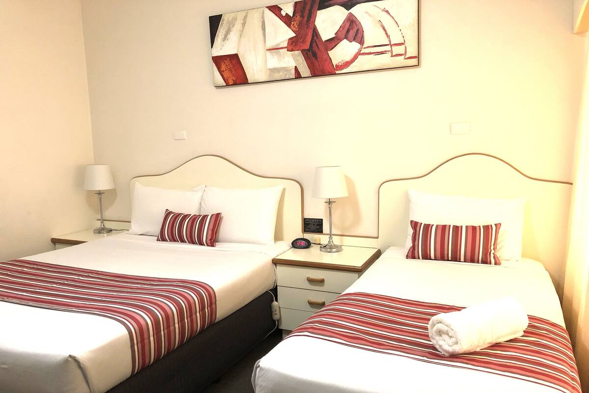 A hotel room with two beds, each with a striped bedspread, white pillows, and a nightstand with a lamp and a clock.