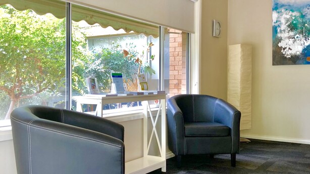 A room with a large window, a desk, two chairs, a carpeted floor, and a painting on the wall.