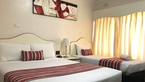 A hotel room with two beds, a nightstand, a lamp, and a painting on the wall.