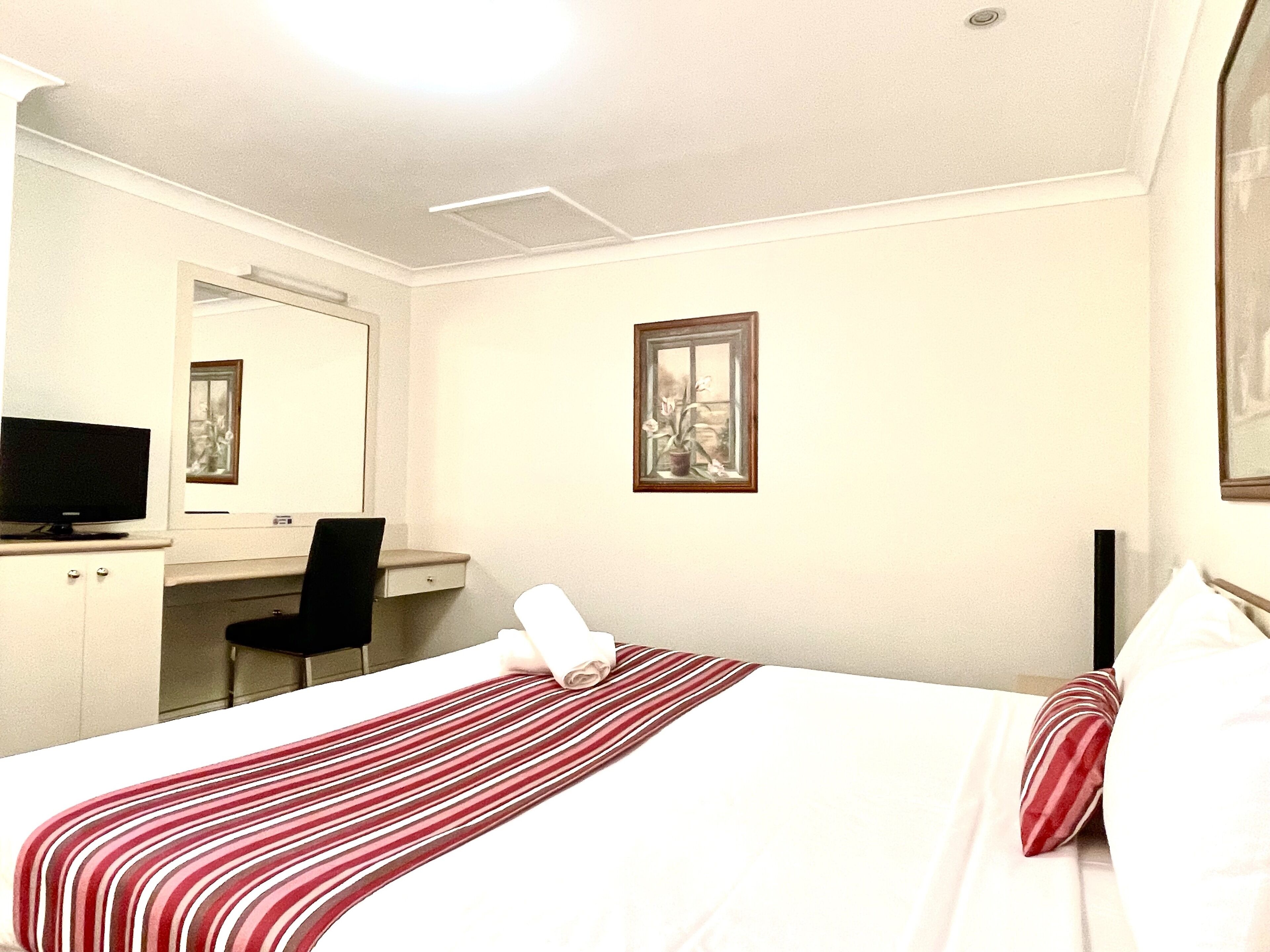 Habitación de hotel con cama, escritorio, silla, televisor y un cuadro en la pared.