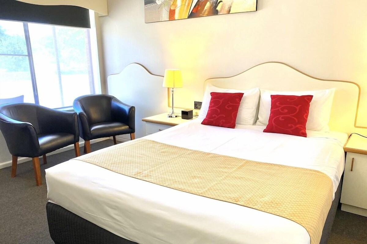 A hotel room with a large bed, two chairs, a nightstand, and a lamp.