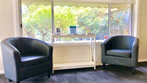 A room with two black leather chairs, a white table with a glass top, and a window with a view of trees and a building.