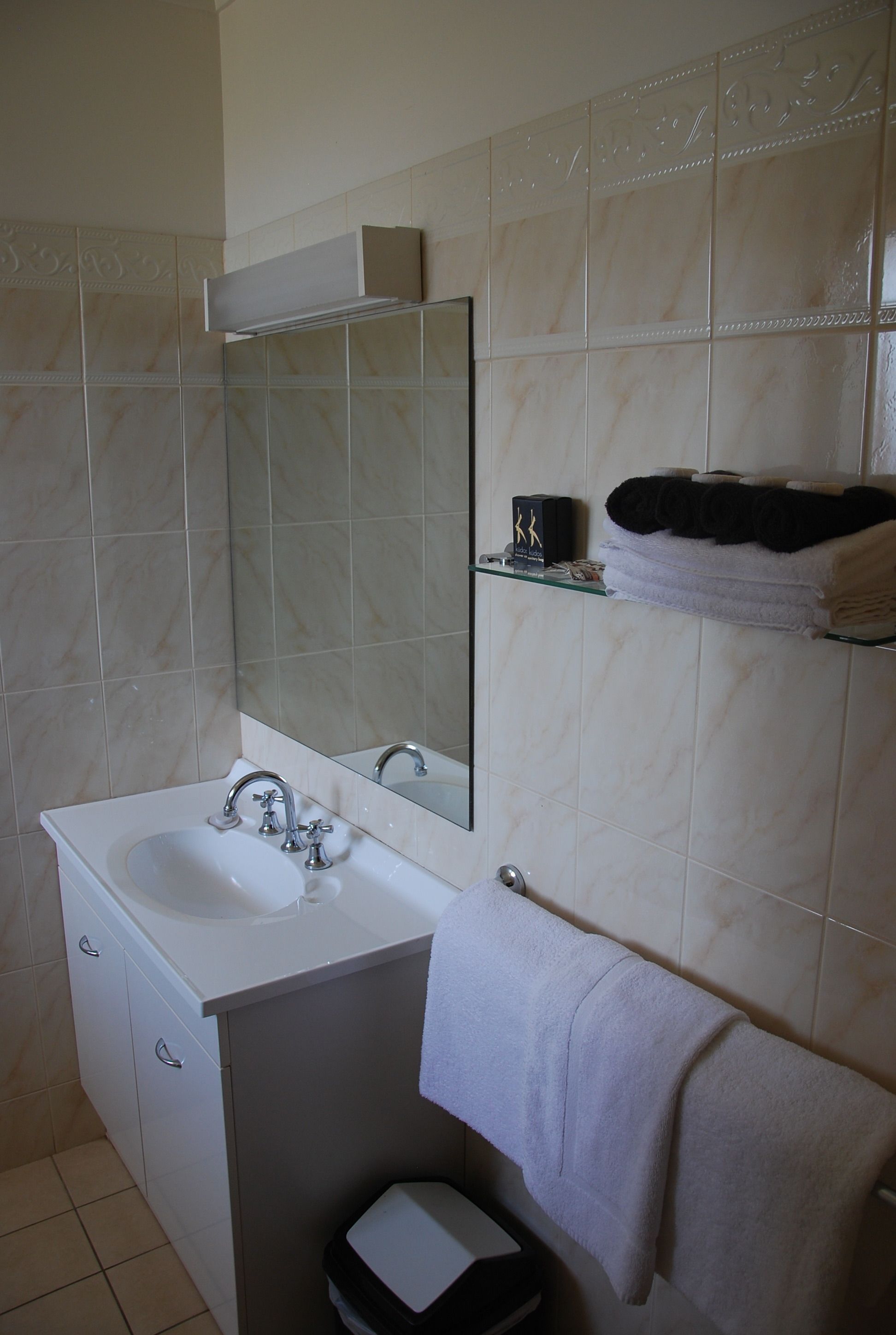 Casa de banho com lavatório branco, espelho e suporte para toalhas.