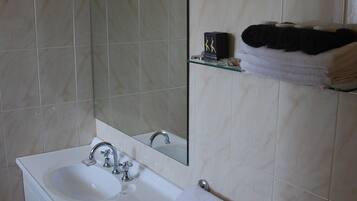 Casa de banho com lavatório branco, espelho e suporte para toalhas.