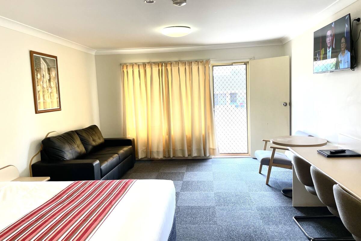 A hotel room with a bed, a black leather sofa, a desk, and a chair.