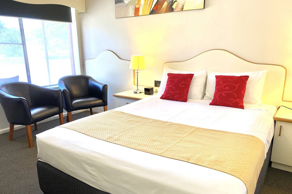 A hotel room with a large bed, two chairs, a nightstand, and a lamp.
