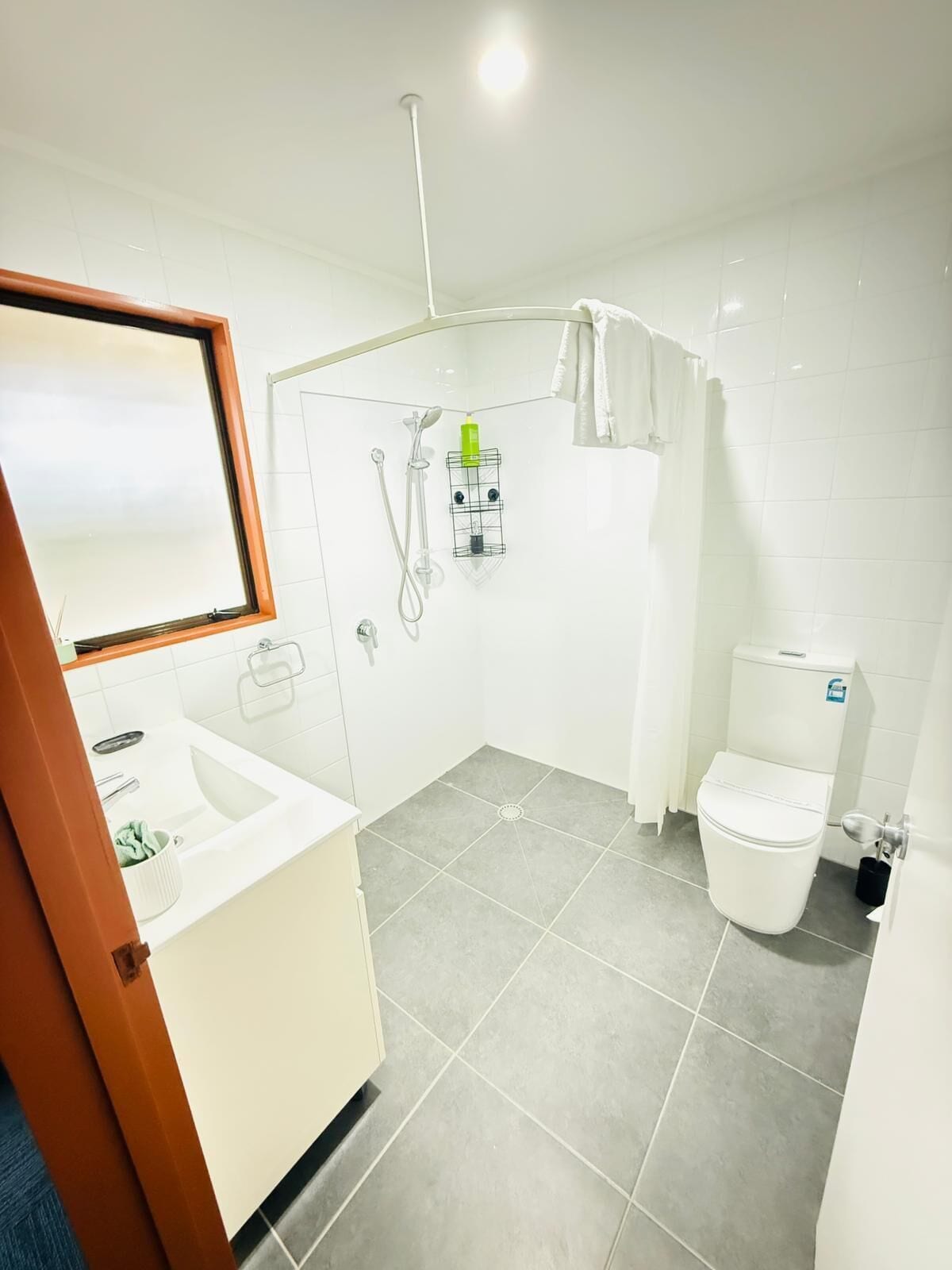 A bathroom with a shower, toilet, sink, and a mirror.