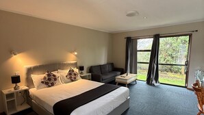 A hotel room with a large bed, a sofa, a small table, and a view of the outdoors through a large window.