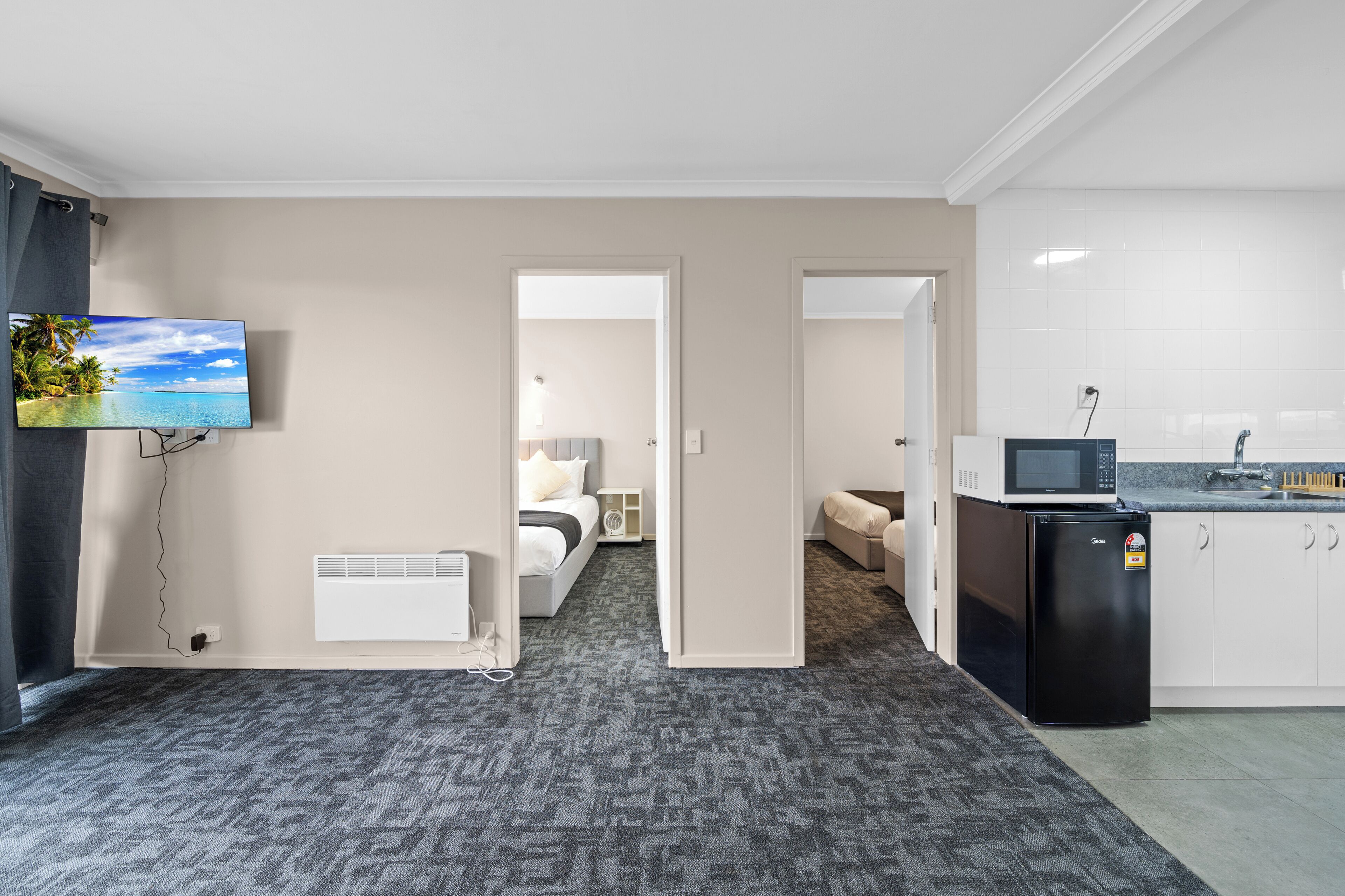 A hotel room with a large TV, a bed, a desk, a microwave, and a refrigerator.