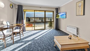 A hotel room with a large sliding glass door to the outside, a wooden desk with a chair, a television mounted on the wall, and a radiator.
