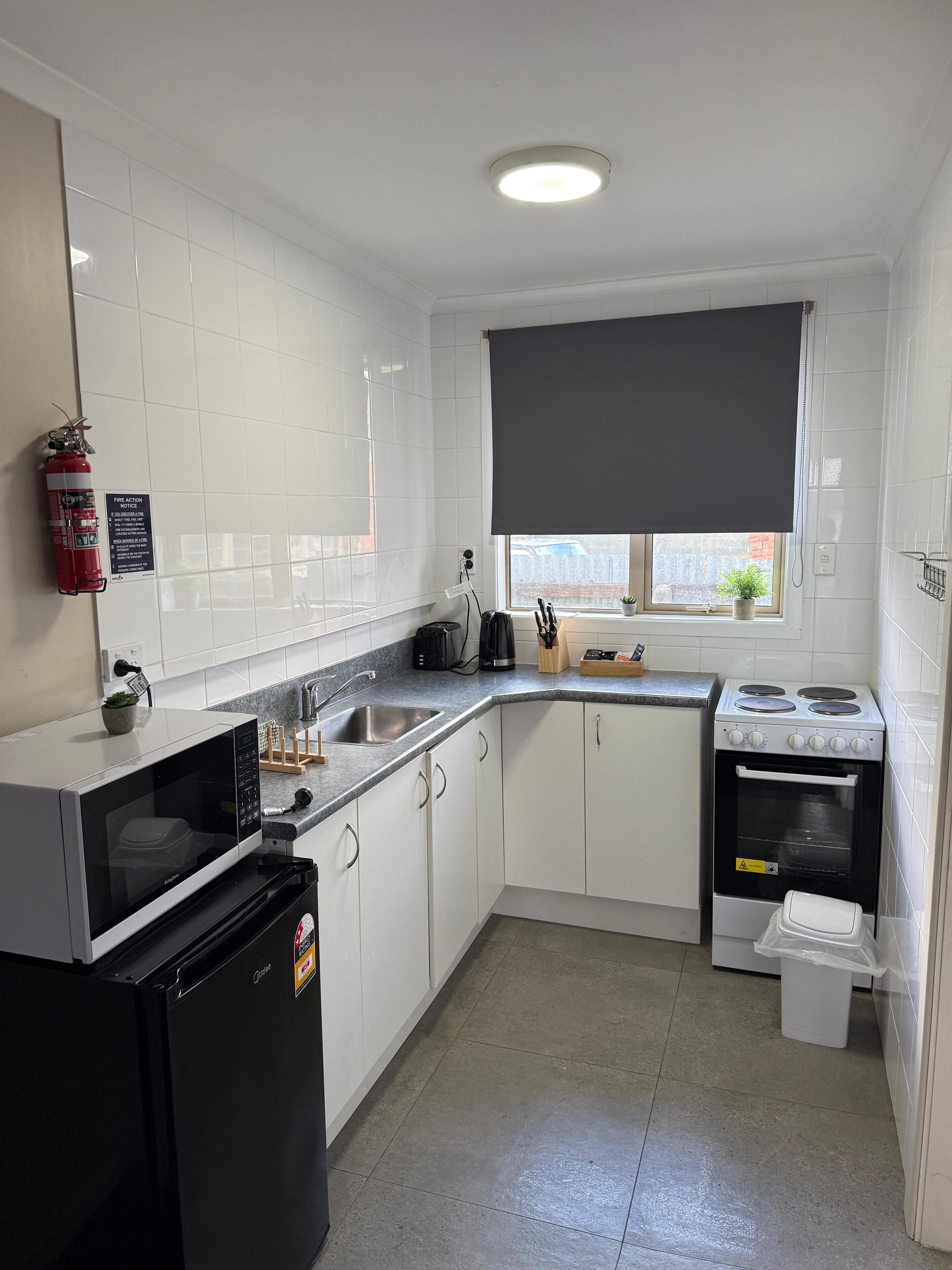 Une cuisine moderne avec des meubles blancs, un réfrigérateur noir, un four à micro-ondes, une cuisinière et un évier.