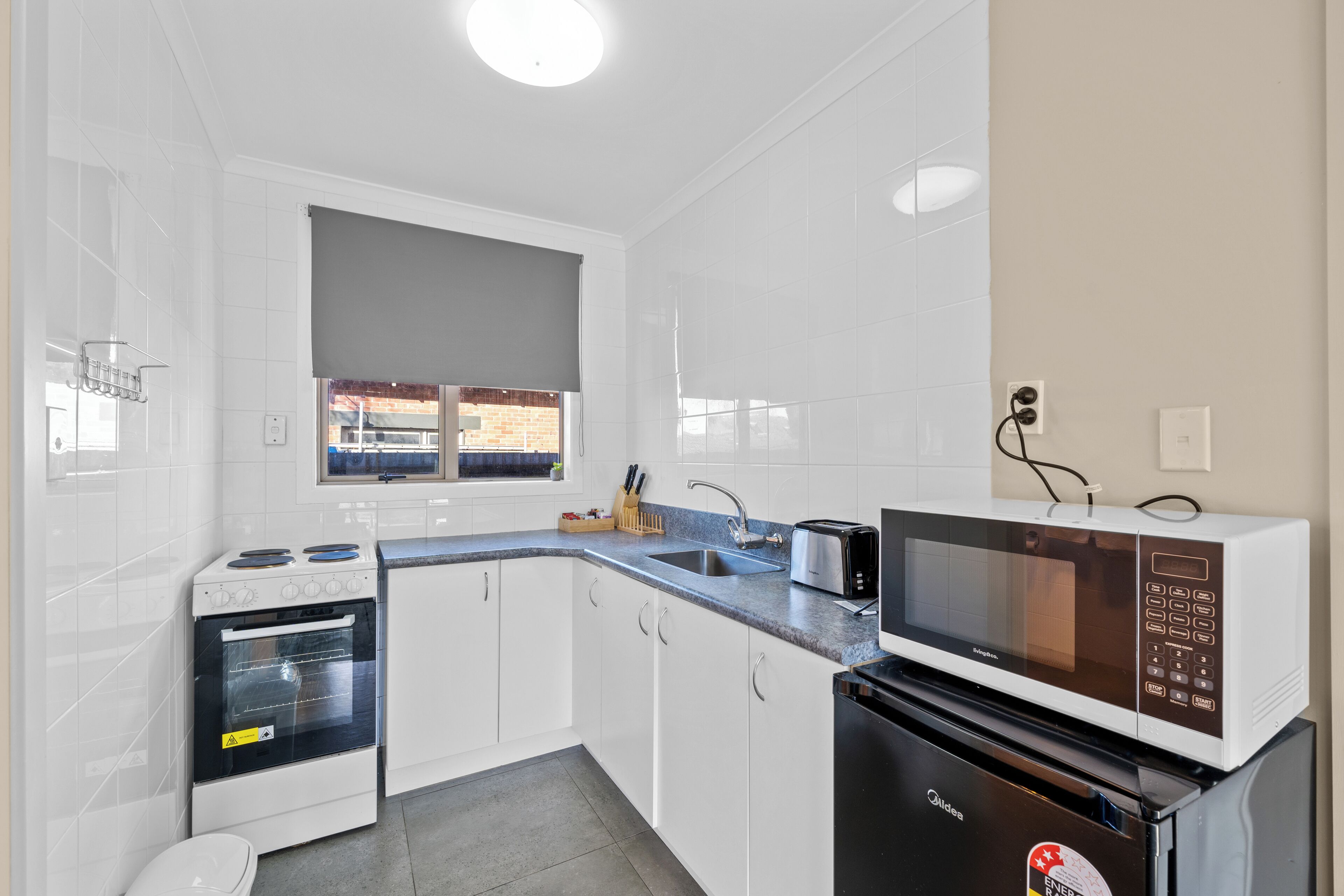 A compact kitchen with white cabinets, a built-in oven, a microwave, and a sink.