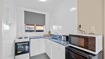 A compact kitchen with white cabinets, a built-in oven, a microwave, and a sink.