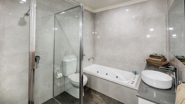Un baño moderno con ducha de vidrio, inodoro blanco, bañera independiente y tocador con lavamanos y una pila de toallas.
