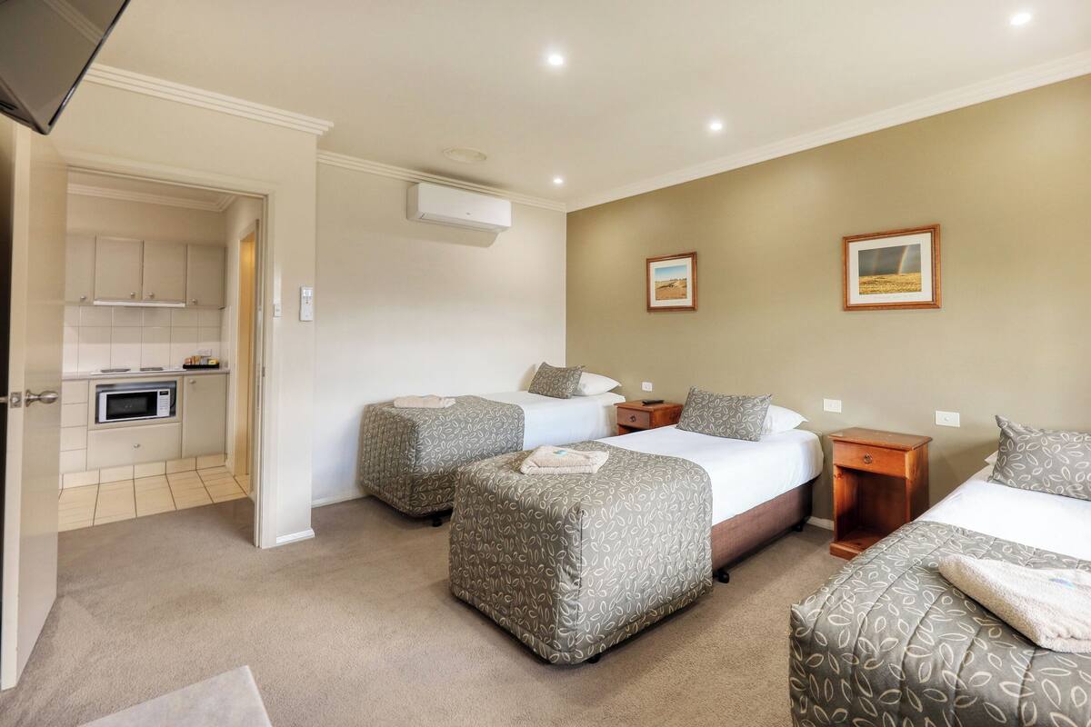 A hotel room with two beds, a kitchenette, and a bathroom.