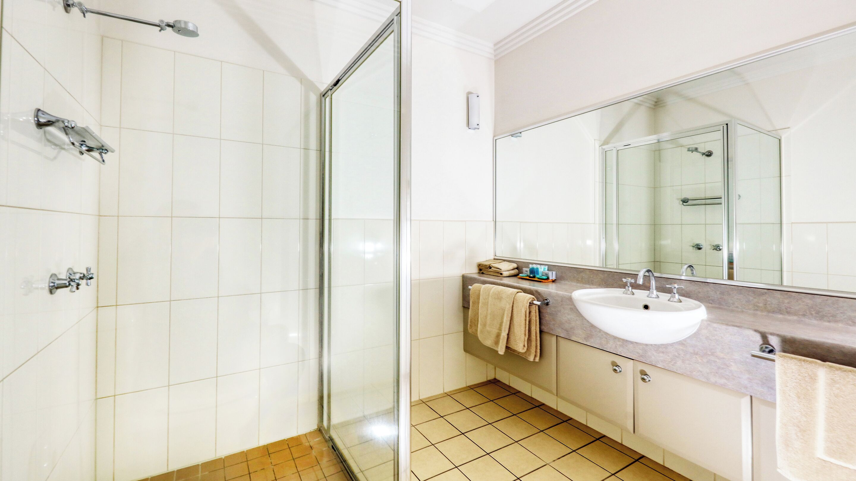 Ein modernes Badezimmer mit einer Duschkabine aus Glas, einem weißen Waschbecken mit Marmorplatte und einem großen Spiegel darüber.