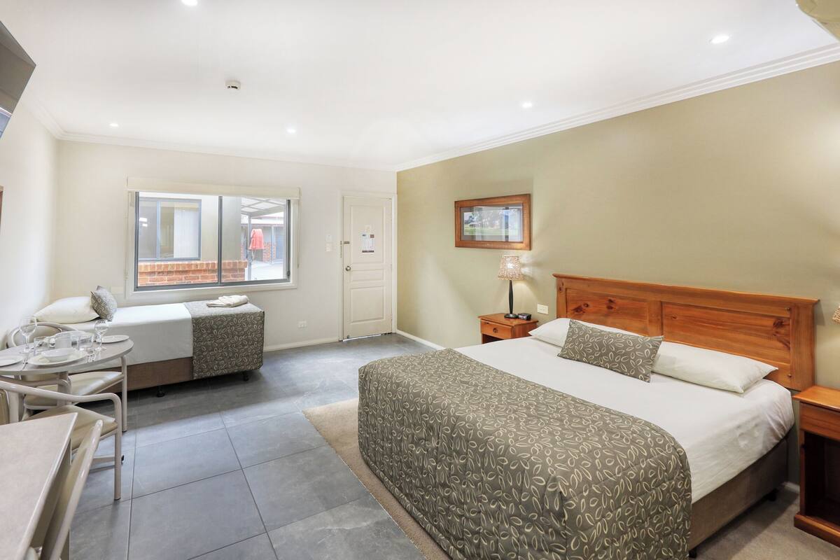 A hotel room with a bed, a desk with a chair, a small table, and a window.