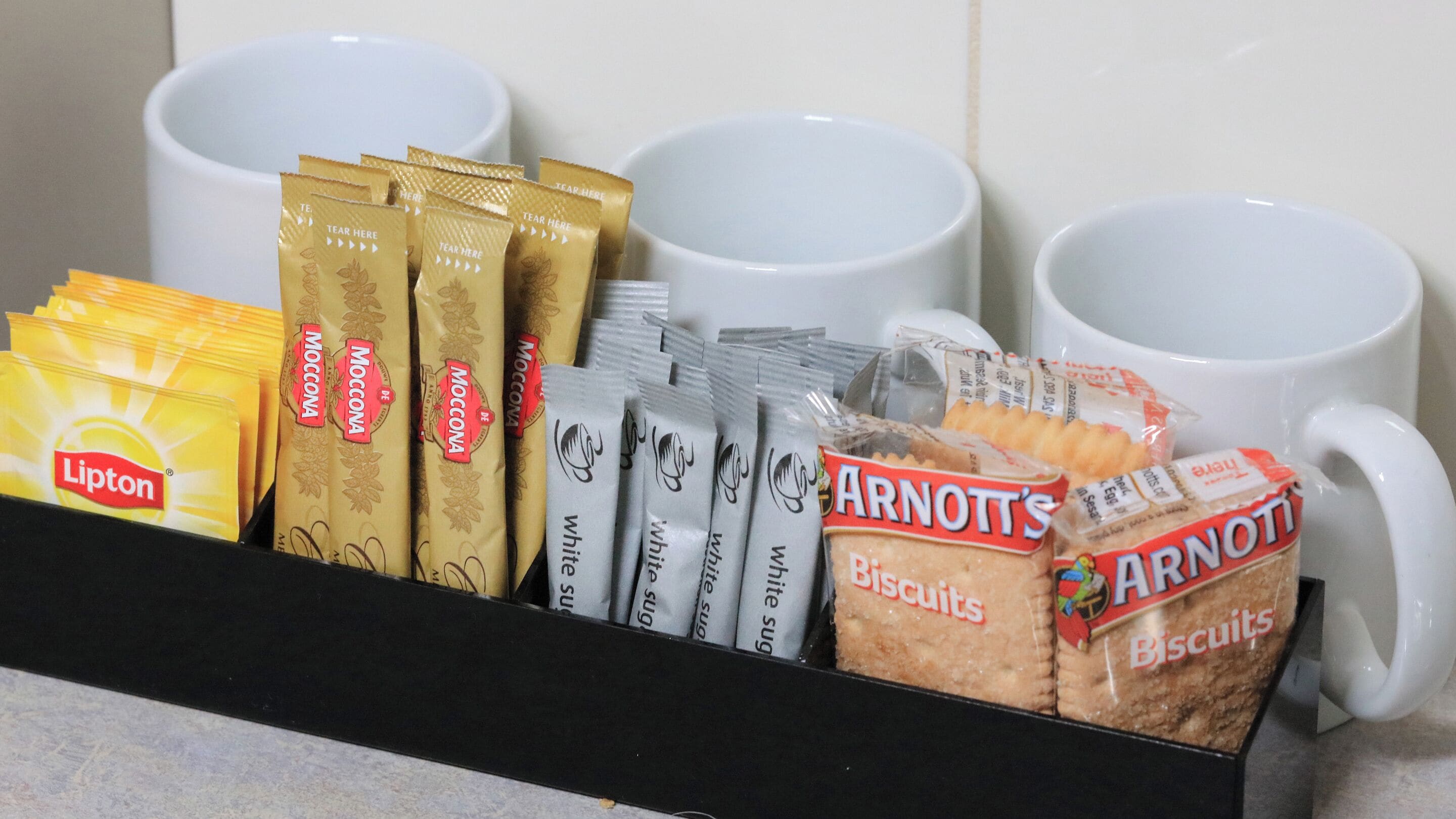 Exhibición de café y galletas con té Lipton, café Moccona, paquetes de azúcar blanco y galletas Arnott's.