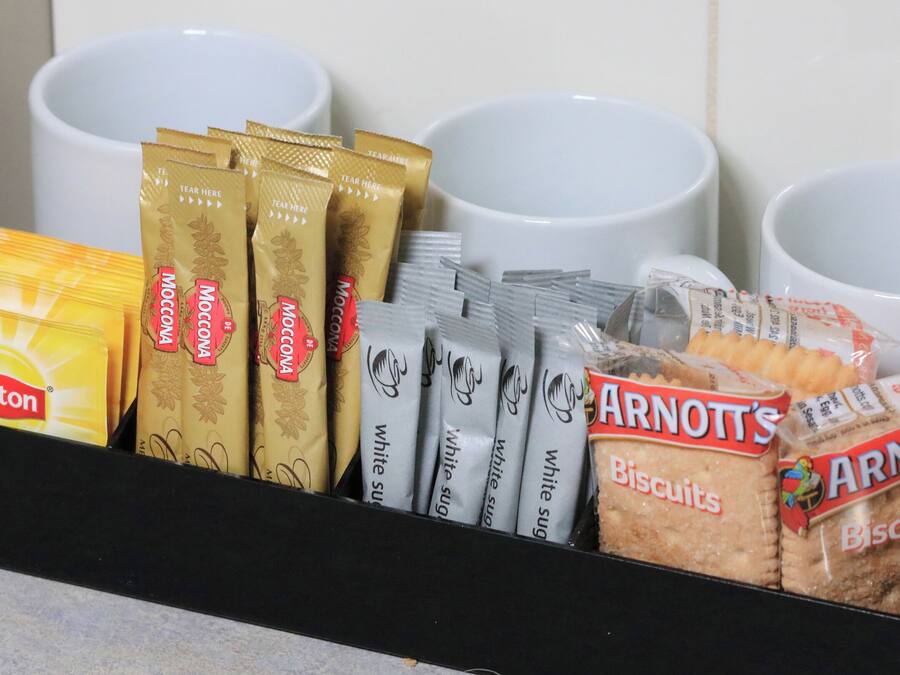 Exhibición de café y galletas con té Lipton, café Moccona, paquetes de azúcar blanco y galletas Arnott's.