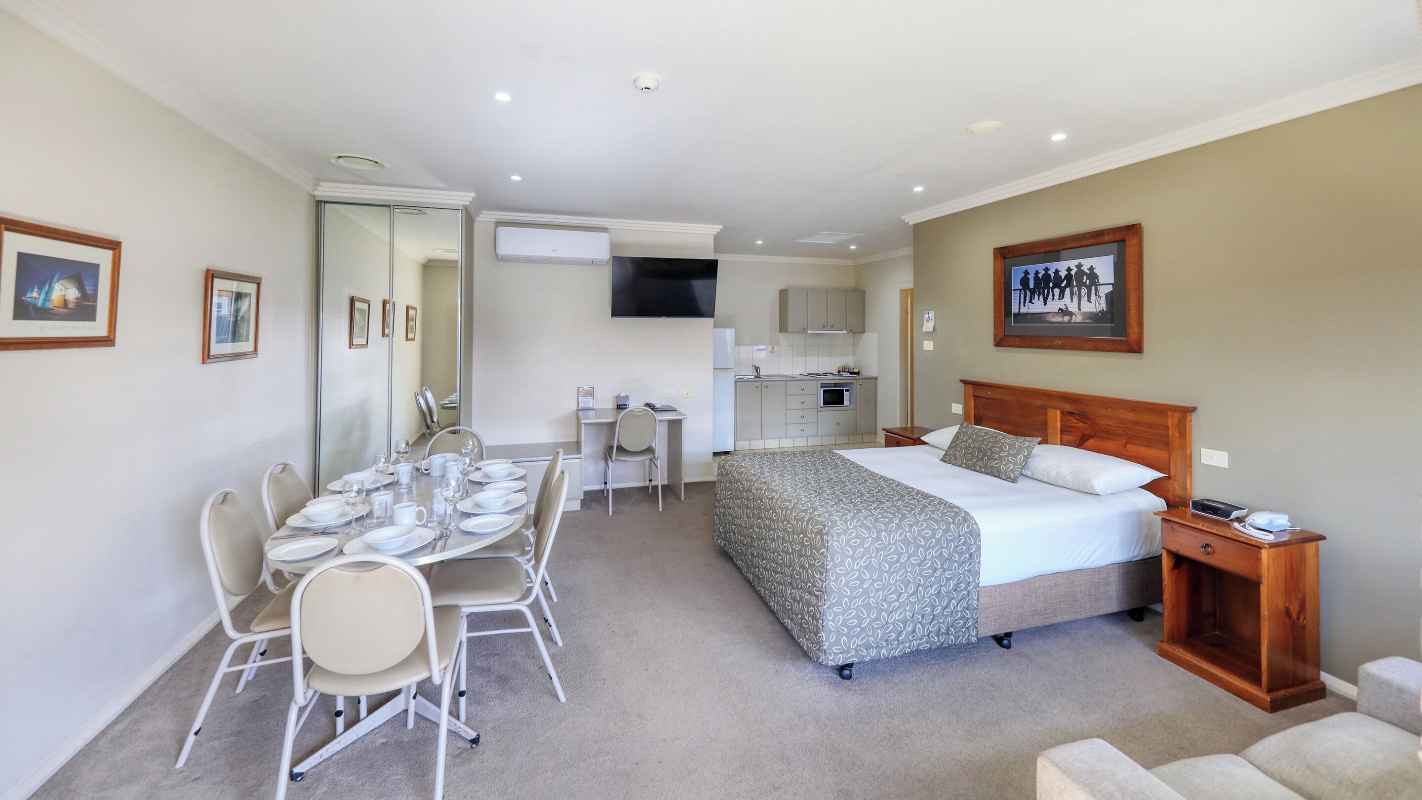 A hotel room with a bed, a desk, a chair, and a dining table set for two.