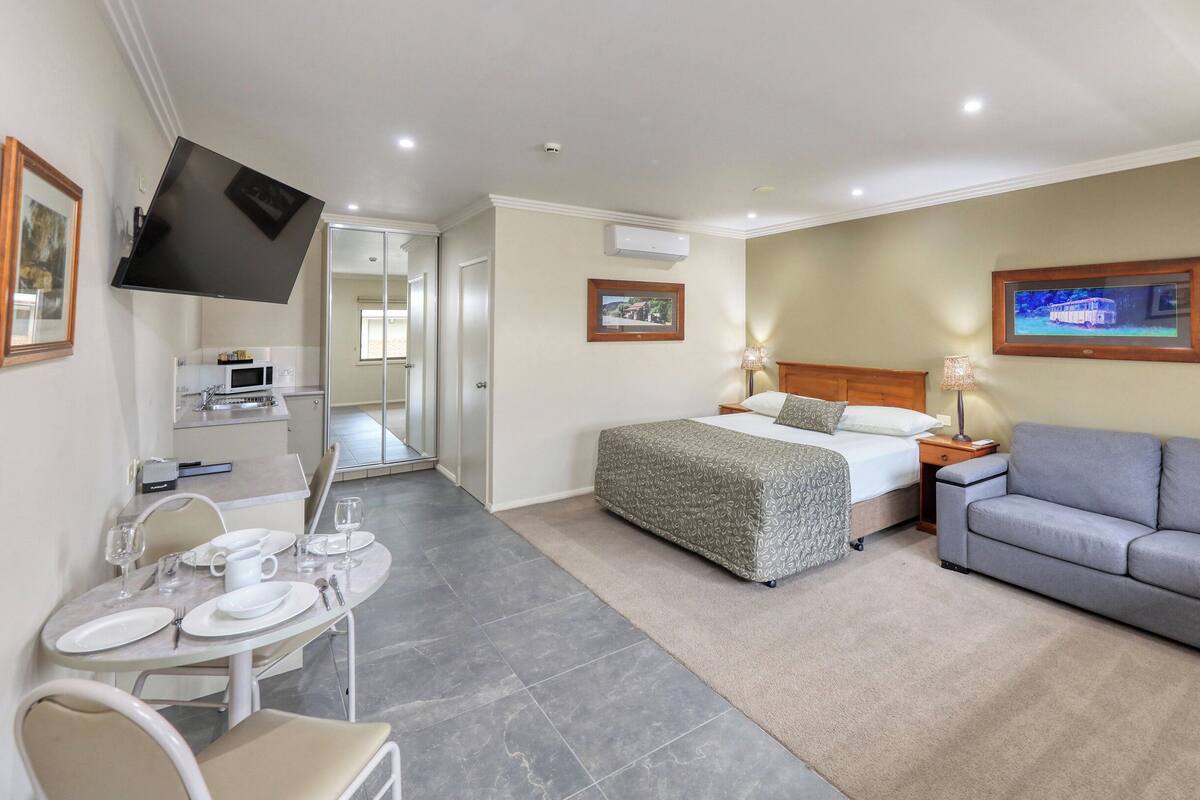 A hotel room with a bed, a sofa, a TV, a desk with a chair, and a dining area.