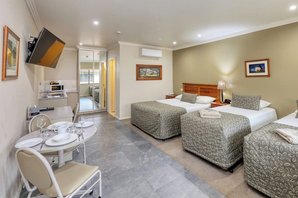 A hotel room with two beds, a dining area with a table and chairs, a kitchenette, and a TV mounted on the wall.