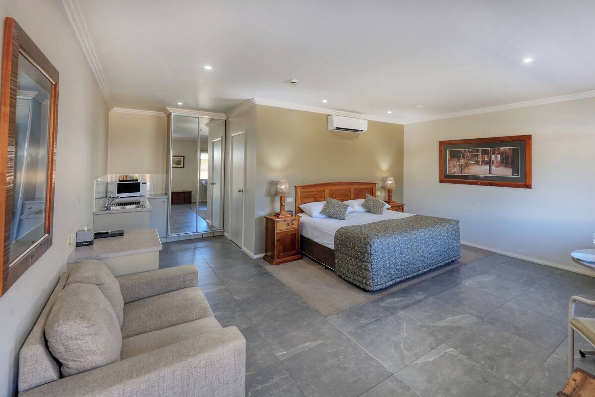 A hotel room with a bed, bedside tables, a TV, a seating area with a sofa and chairs, and a small table with glasses and plates.