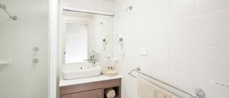 Un baño con cabina de ducha de vidrio, un lavamanos blanco con espejo y un perchero en la pared.