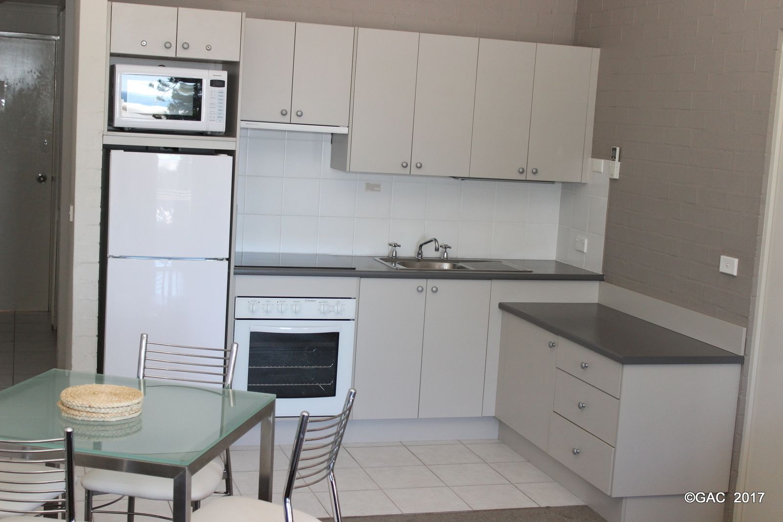 A compact kitchen with white cabinets, a microwave, a refrigerator, an oven, a sink, and a dining table with chairs.