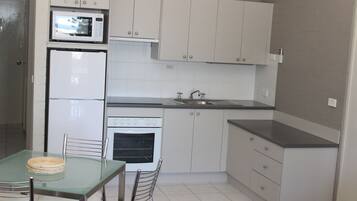 A compact kitchen with white cabinets, a microwave, a refrigerator, an oven, a sink, and a dining table with chairs.