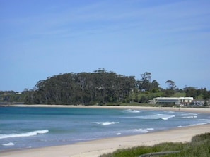 A beach with clear blue water, a sandy shore, and a forested hill in the background. - Mollymook Cove Apartments (Mollymook)