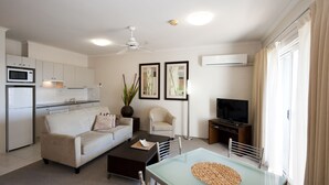 A modern living room with a sofa, coffee table, TV, and dining area. - Mollymook Cove Apartments (Mollymook)