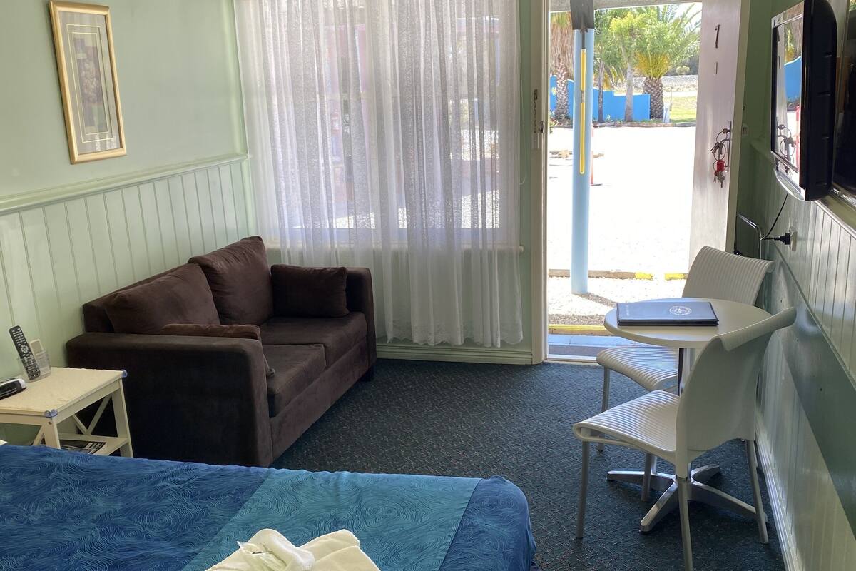 Une pièce comprenant un lit, un canapé, une petite table, une chaise et une fenêtre avec des rideaux.