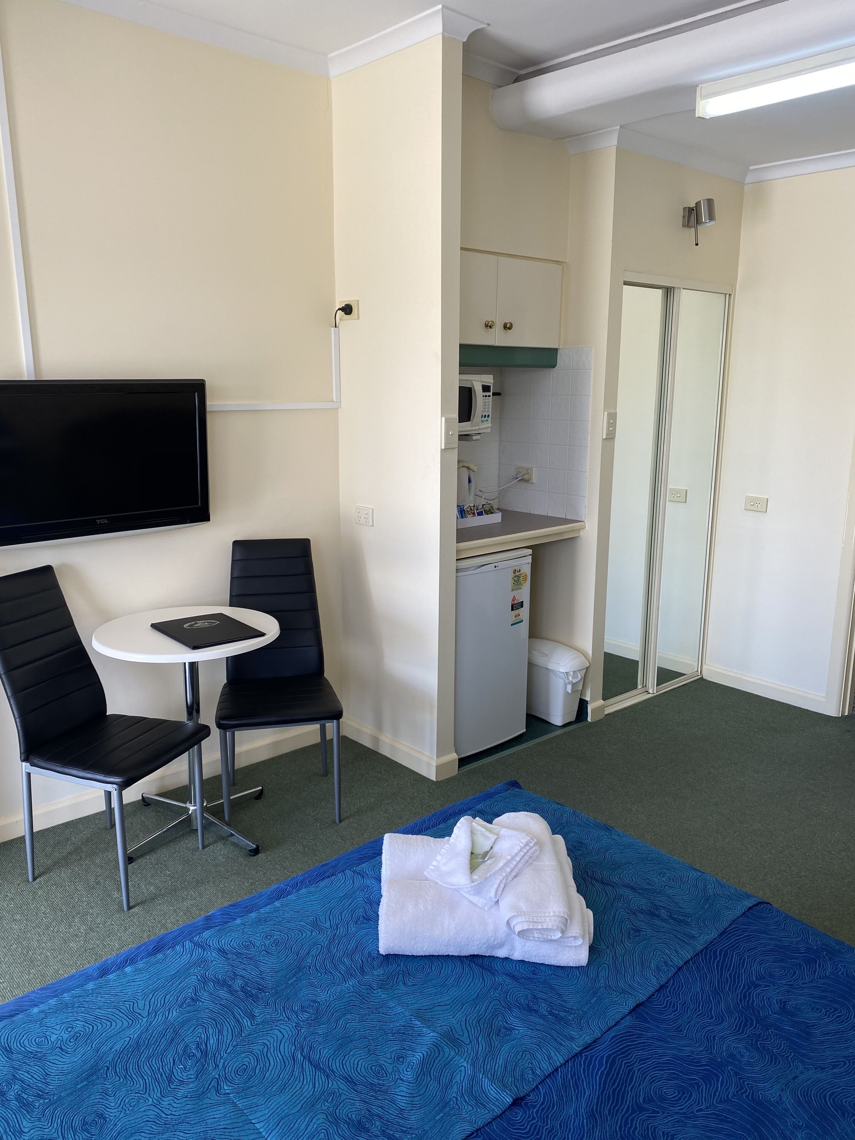 A hotel room with a bed, a small table with two chairs, a TV, a kitchenette, and a bathroom.