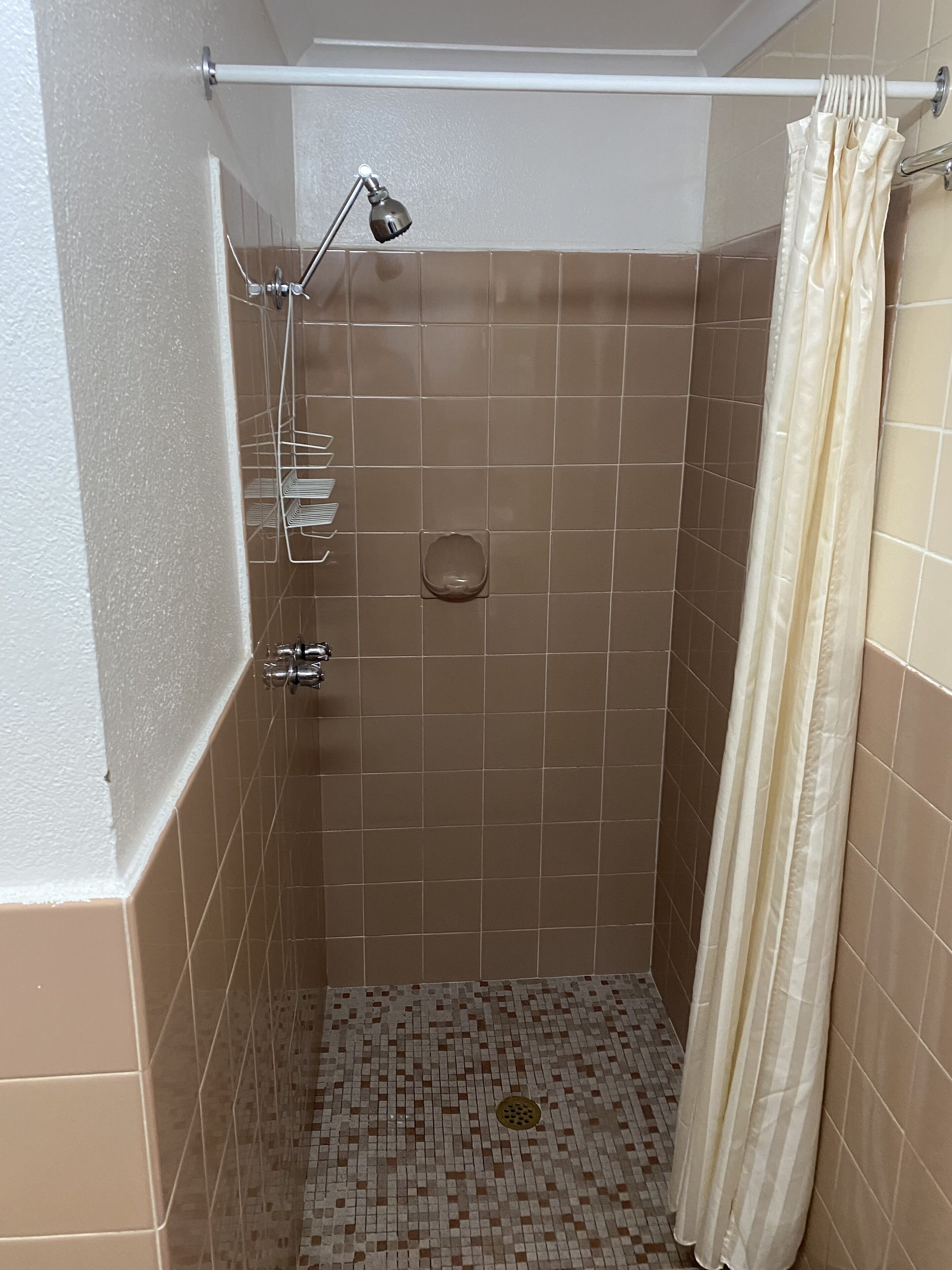 Un pequeño box de ducha con azulejos, un cabezal de ducha, una cortina y un pasamanos.