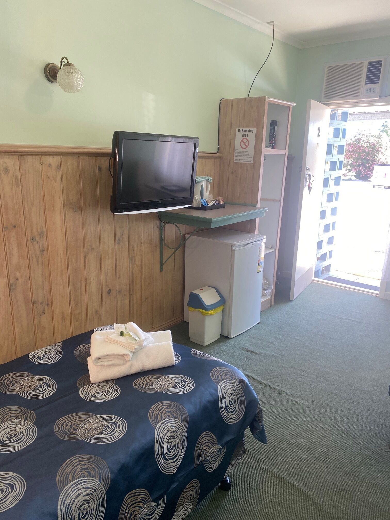 Une chambre d’hôtel équipée d’un lit, d’une télévision, d’un petit réfrigérateur et d’une poubelle.