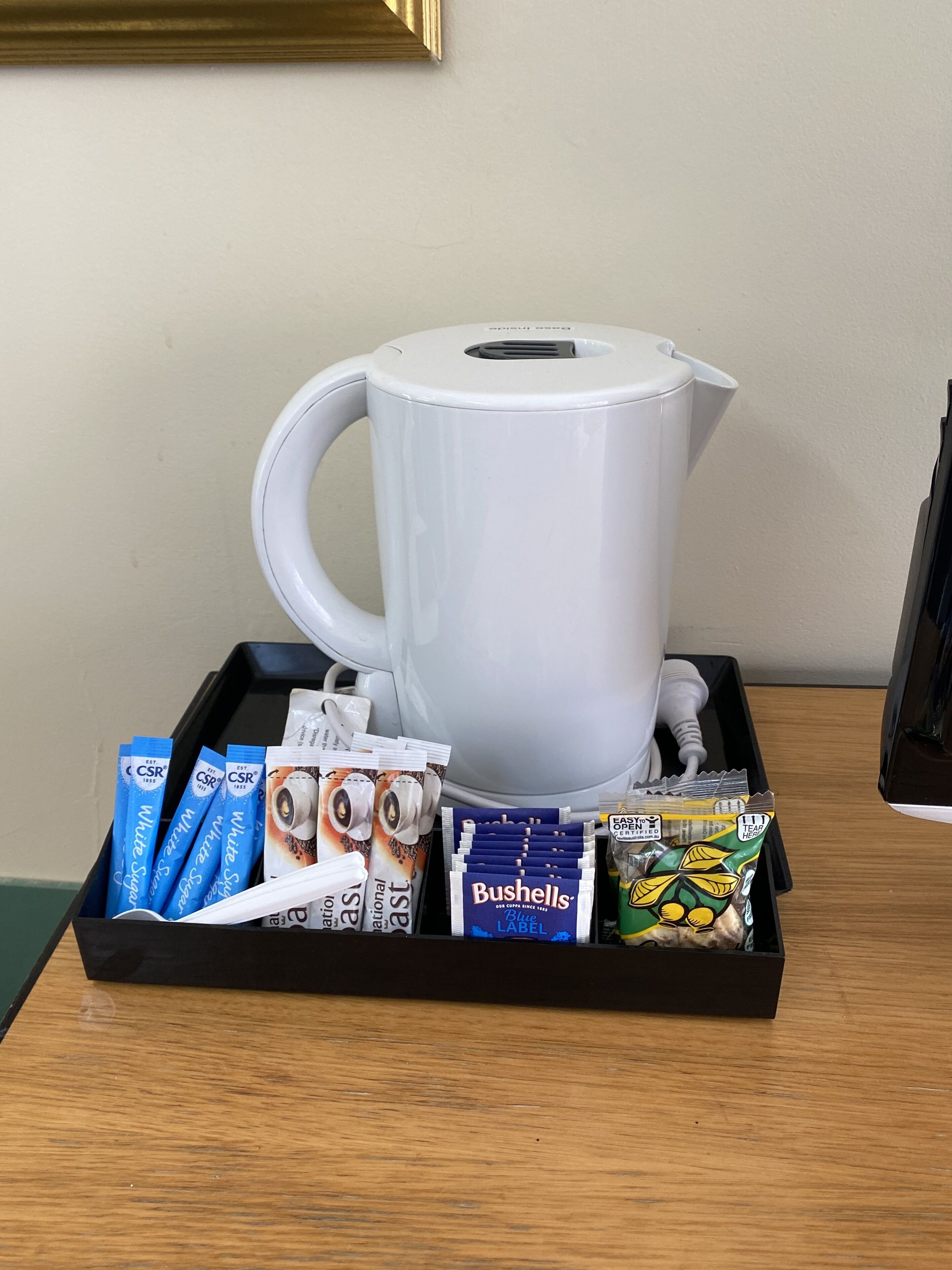 A tray with a white coffee maker, coffee pods, a box of Bushells tea bags, and a green tea bag.