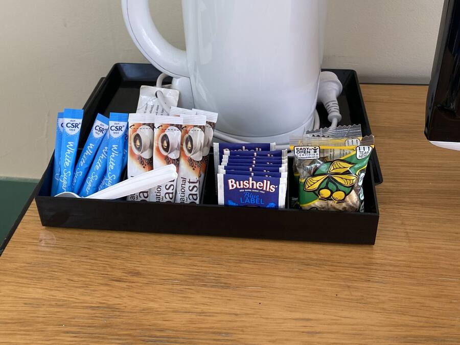 A tray with a white coffee maker, coffee pods, a box of Bushells tea bags, and a green tea bag.