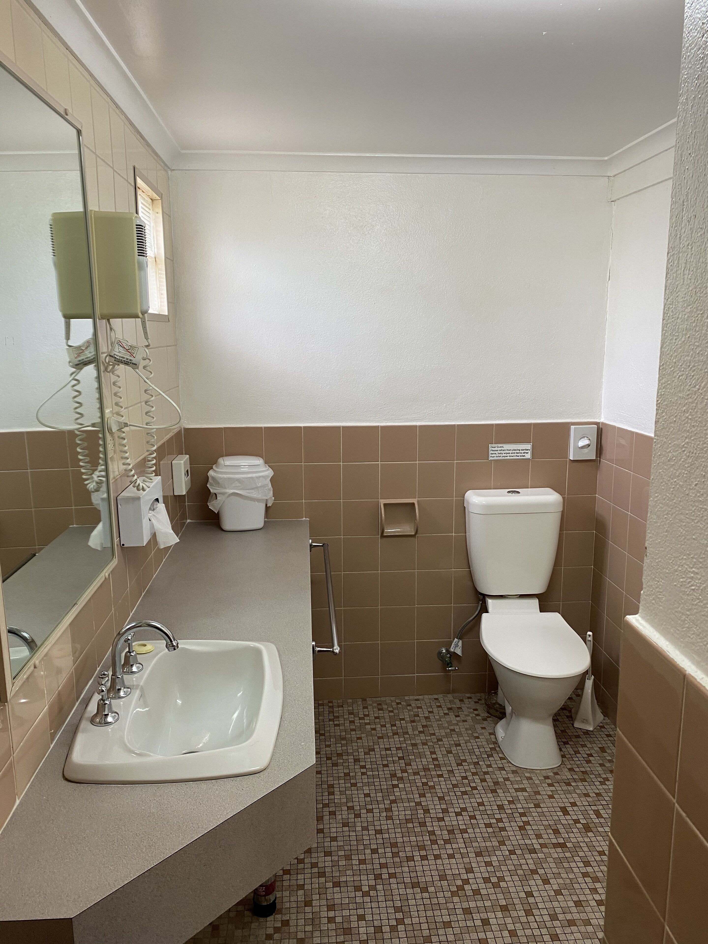 A bathroom with a sink, mirror, toilet, and hand dryer.