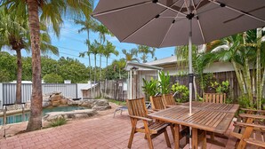 Un patio con mesa y sillas de madera, una sombrilla grande y una piscina pequeña.