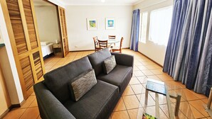 Una sala de estar con sofá, ventilador de techo, mesa de comedor con sillas y ventana con cortinas.