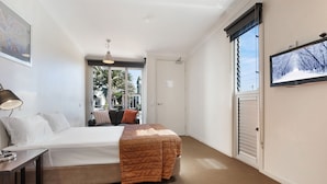 Un dormitorio con cama, mesita de noche, lámpara y televisor en la pared.