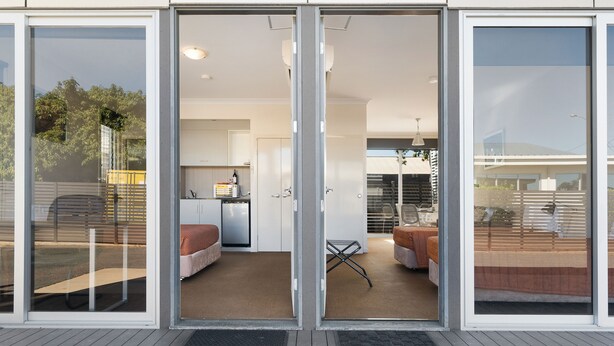 Un edificio moderno con puerta de vidrio corredera que da acceso a un interior bien iluminado, con cocina, zona de estar y vistas al exterior.
