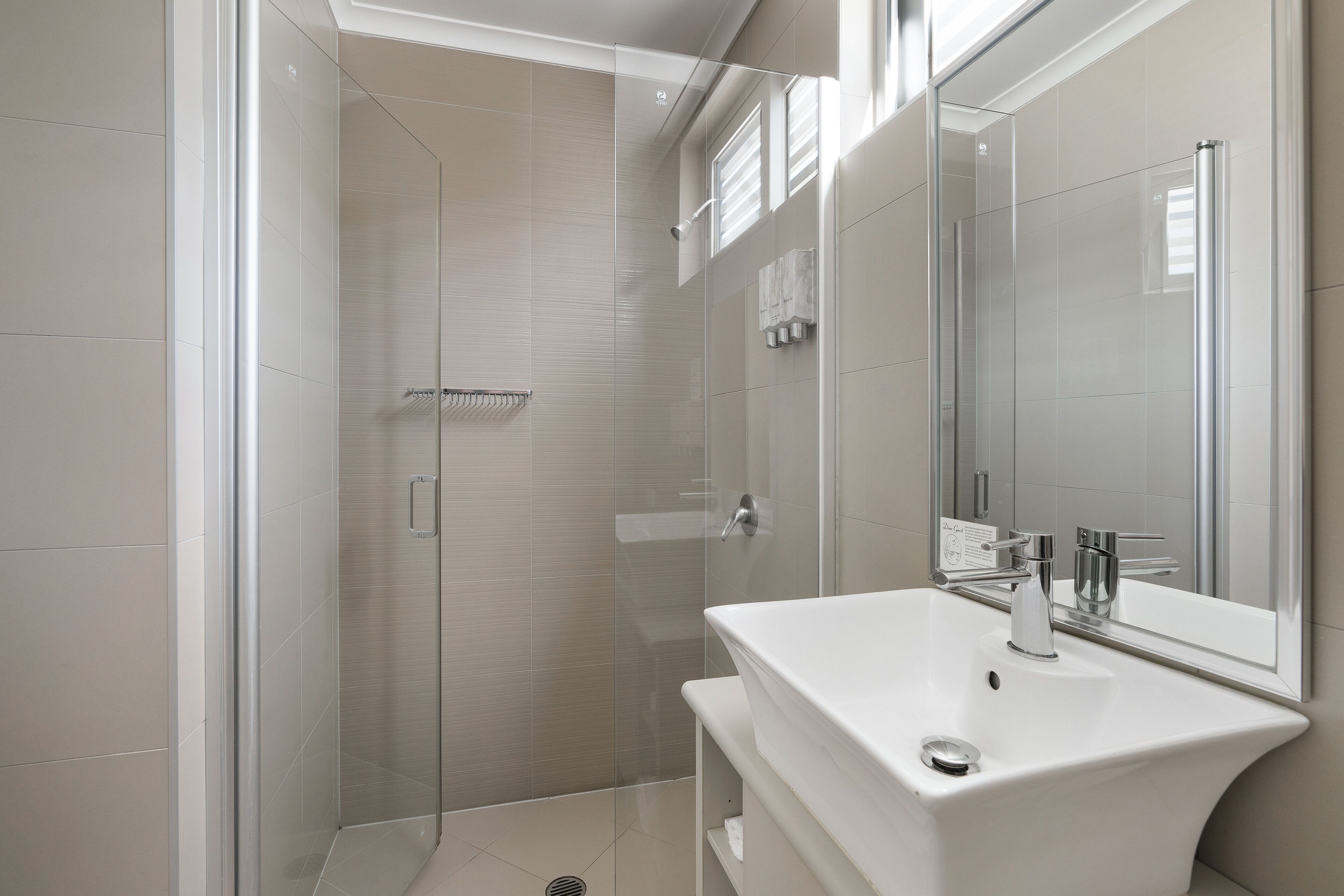 A modern bathroom with a glass-enclosed shower, a white sink, and a large mirror.