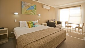 Una habitación de hotel con una cama grande, un ventilador de techo, un cuadro, un escritorio y una ventana con persianas.