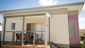 A modern mobile home with a covered patio area, a dining table, and chairs.