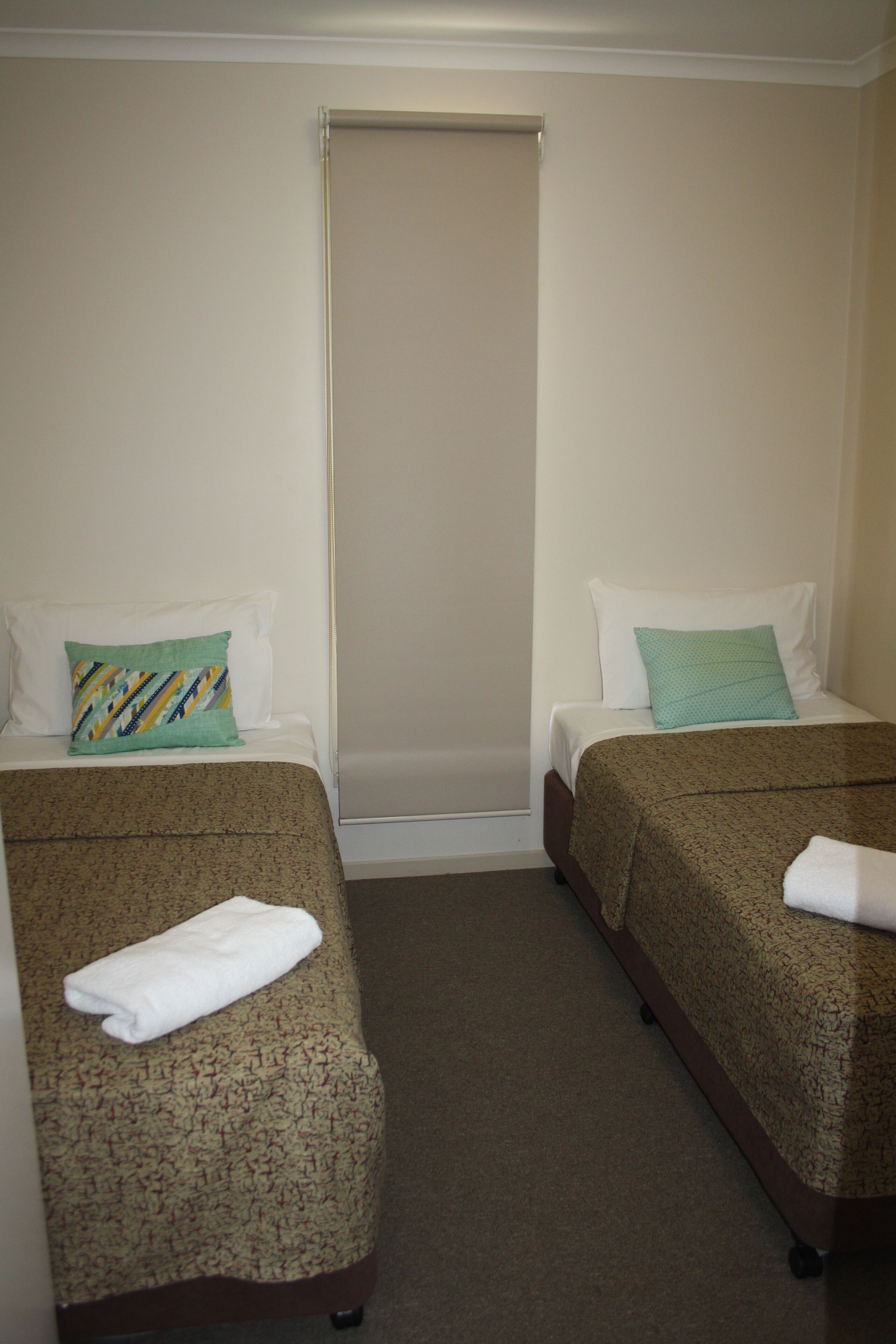 A hotel room with two beds, each with a patterned bedspread and a pillow.