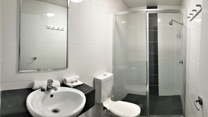 Un baño moderno con un lavamanos blanco, inodoro y ducha con mampara de cristal.